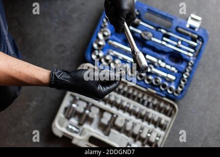 From above anonymous male technician in latex gloves selecting wrench bit from tool box during work in garage Stock Photo