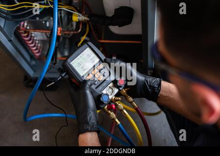 Male mechanic in goggles and gloves using voltage tester on modern machine during work in workshop Stock Photo