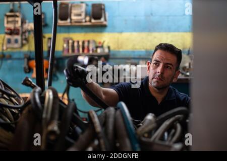 Professional adult male mechanic taking hose for painting car from storage while working in repair service workshop Stock Photo