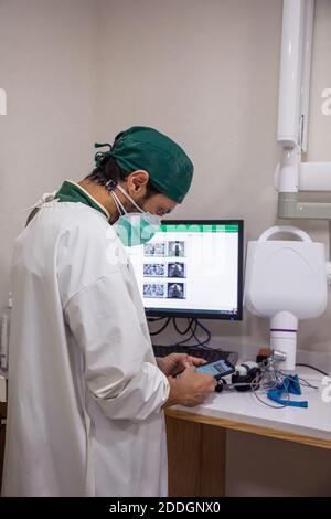 Side view of male dentist in mask and uniform using cellphone while working in modern dental hospital Stock Photo