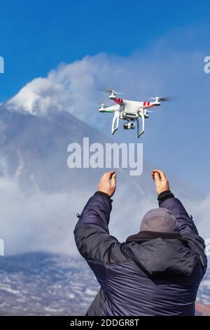 Male launches flying drone quadcopter UAV with digital camera on background of volcano eruption, mount peak erupting ashes, volcanic gas from crater Stock Photo