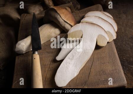 From above composition of raw whole and sliced porcini or cep mushrooms with knife and cutting board on wooden rustic table Stock Photo
