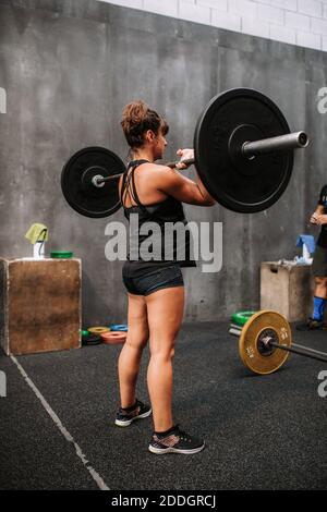 Back view of athletic pregnant Woman doing exercises with barbell in gym during workout Stock Photo