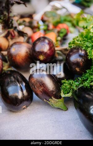 Bunch of natural bio fresh mini eggplants placed on table with vegetables and greenery on counter on marketplace Stock Photo