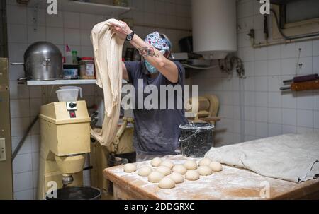 Unrecognizable female baker in mask working in bakery and kneading raw dough while cooking delicious bread Stock Photo
