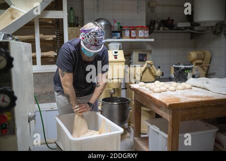 Unrecognizable female baker in mask working in bakery and kneading raw dough while cooking delicious bread Stock Photo