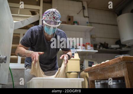 Unrecognizable female baker in mask working in bakery and kneading raw dough while cooking delicious bread Stock Photo