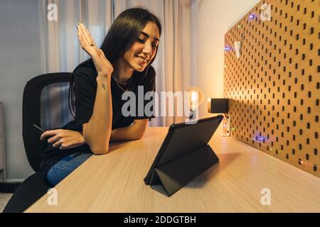 An attractive Caucasian woman having an online video chat with friends via tablet rising her hand Stock Photo