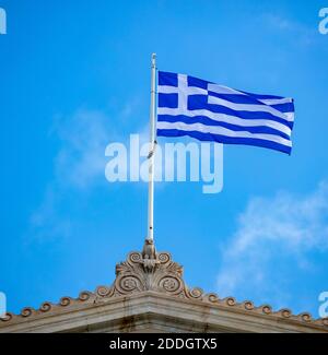 Greek flag waving on pole against clear blue sky background, copy space. Greece national sign symbol on Parliament building top Stock Photo