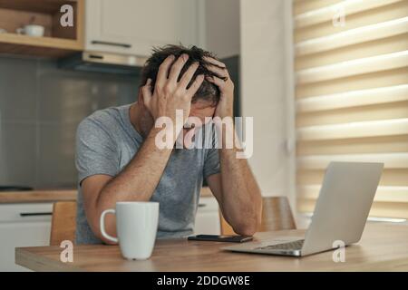 Disappointed freelancer at home office having job problems with his head in hands, selective focus Stock Photo