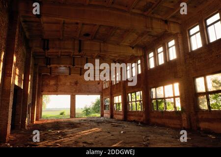 A large abandoned industrial building is lit by light from the windows. Large red brick building. Stock Photo