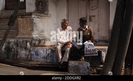 Two men are sitting and having a conversation on a street corner in Bundi, India. Stock Photo