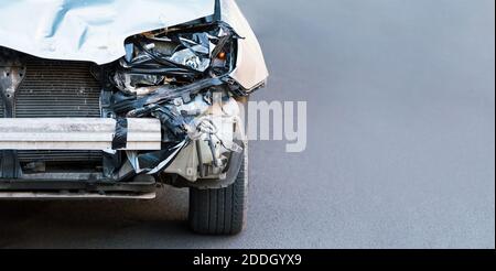 Destroyed car in car crash traffic accident on city road with copy space. Smashed broken front auto headlight, dented hood without bumper on gray car Stock Photo