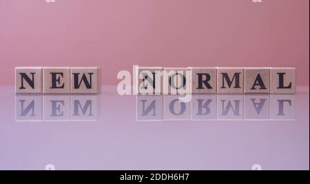 Text NEW NORMAL on wood cube blocks. The letters NEW NORMAL written on the cubes in black letters isolated on a glass surface. NEW NORMAL text for yo Stock Photo