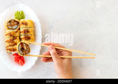 Japanese sushi food on white background with copy space. Female hand holding sushi. Top view of sushi in white plate. Soft focus Stock Photo