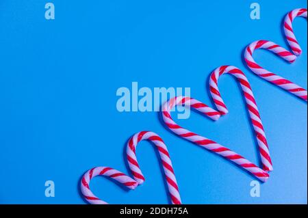 Candy caramel cane in the form of a heart on a blue background. Christmas concept, New Year, minimalism. Flat lay, top view Stock Photo
