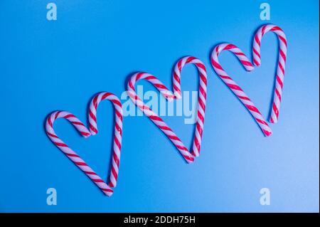 Candy caramel cane in the form of a heart on a blue background. Christmas concept, New Year, minimalism. Flat lay, top view Stock Photo