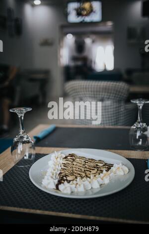 a vertical shot of a white cake with black topping on a white plate on a restaurant table Stock Photo