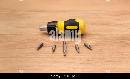Yellow-black handle screwdriver and bit set still life on wooden backdrop. Detailed macro photography with using focus stacking method. Stock Photo