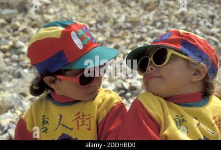 two little sisters in coloured caps and sunglasses looking at each other with attitude Stock Photo