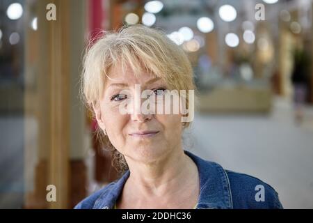 Portrait of serious attractive old lady who is walking in the shopping mall. Aged blond woman in the trade gallery. Stock Photo