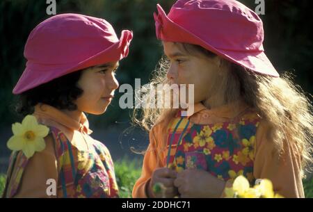 two sisters in pink hats face to face in garden of daffodils Stock Photo