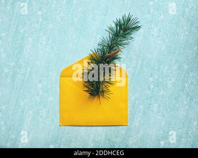 Christmas or New Year composition. Paper yellow envelope with a spruce branch on a blue background. Flat lay style. New Year greeting card. Stock Photo