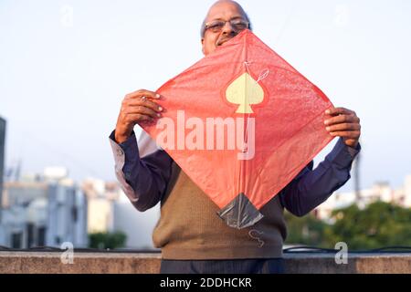 Man with glasses holding a red and yellow kite aloft on the indian festival of makar sankranti uttarayana Stock Photo