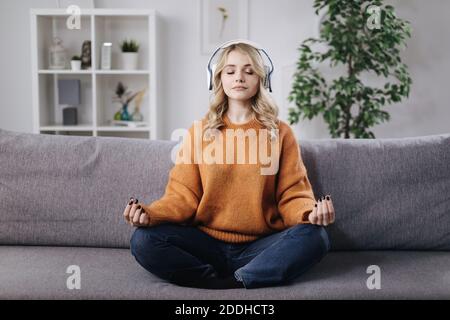Woman meditating in headphones on couch Stock Photo