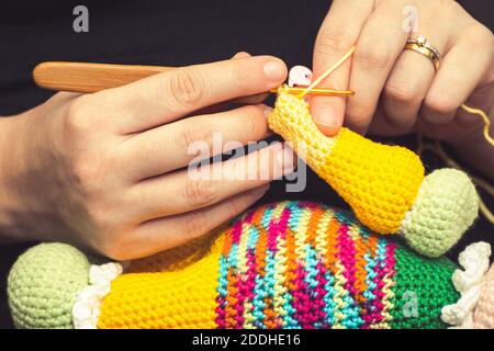 Close up on the hand of a woman using a knitting needle to sew a crochet doll with a woolen yarn. Stock Photo