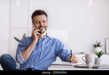 Handsome Businessman Talking On Cellphone And Taking Notes While Working In Office Stock Photo
