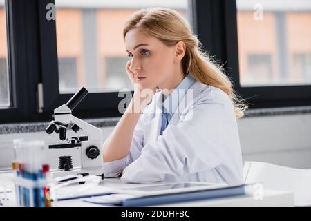 sad scientist leaning on hand near microscope in lab Stock Photo