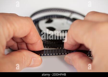 Hands holding a 8mm film strip with roll in background. Close up image with shallow depth of field. Stock Photo