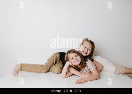 Cheery siblings lie together on a table in opposite directions. Boy hugs girl Stock Photo