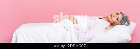 Young woman in pajamas lying on pillow with blanket on pink background, banner Stock Photo