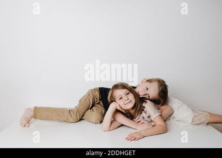 Brother and sister lie together on a table in opposite directions. Boy hugs girl Stock Photo