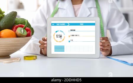 Black female dietologist doctor holding digital tablet with daily calories counting app Stock Photo
