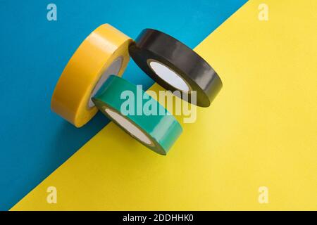 Set of multicolored rolls of electrical round adhesive sticky insulation tape roll on blue and yellow background Stock Photo