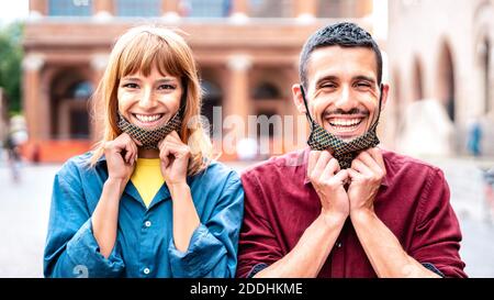 Happy couple smiling with opened face mask after lockdown reopening - New normal relationship concept with guy and girl having fun together Stock Photo