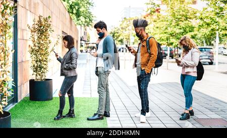 Young people waiting in line practising social distancing at city shop - New normal lifestyle concept with people wearing face mask on urban queue Stock Photo