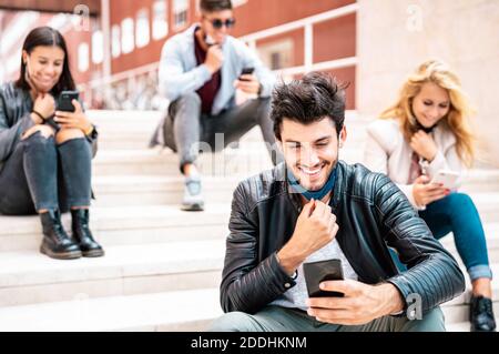 Happy millennial friends smiling with open face mask after lockdown reopening - Happy guy watching news on mobile smart phone Stock Photo