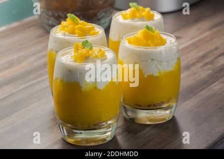 Mango dessert in glasses with cardamom spiced cream and mint sprigh decoration on kitchen top Stock Photo