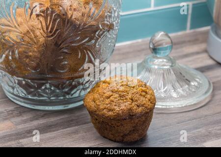 Carrot, apple, cinnamon, pumpkin seed muffin on kitchen countertop next to glass jar with muffins Stock Photo