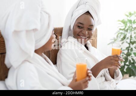 Two joyful black women drinking fresh juice in bed Stock Photo