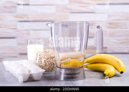 Oat pancakes with banana. Step by step cooking process. Ingredients top view. Bananas, milk, eggs, oats, salt. Wooden table background. Copy space Stock Photo