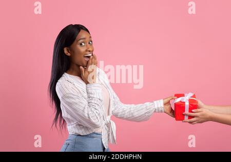 Surprised young lady receiving gift from female friend on pink studio background Stock Photo