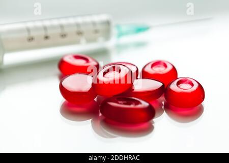 Bunch of red pills & syringe with needle,isolated on white surface with reflection,cure & medication for Coronavirus COVID-19 virus disease,hope Stock Photo
