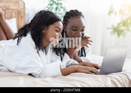 Happy black women in bathrobes using laptop at home, websurfing Stock Photo