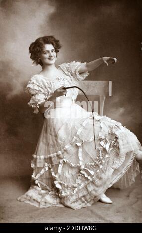 The notable Edwardian English actress and singer Lily Elsie (1886 – 1962) pointing whilst sitting holding a whip, taken from a photographic postcard from the era. Stock Photo