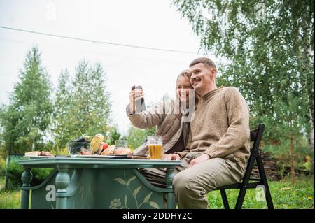 A young couple quarantined during covid-19 at their country home get in touch via video call with their parents. Picnic in nature on self-isolation Stock Photo